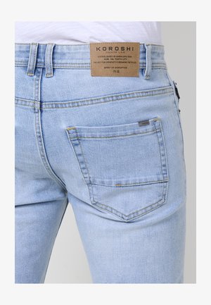 Svetlo modri traper hlače s ožjim krojem, ki imajo usnjeno oznako na pasu in zadnji žep z kontrastnim šivanjem.