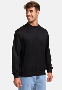 Sudadera negra hecha de un tejido suave, con cuello redondo y mangas largas, combinada con jeans de denim azul claro.