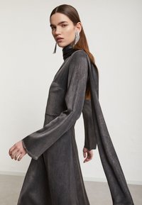 Dlhý rukáv, tmavosivý šaty s vysokým golierom, voľne splývajúci šálový detail a široké rukávy. Hladká textúra s minimálnymi dizajnovými prvkami.