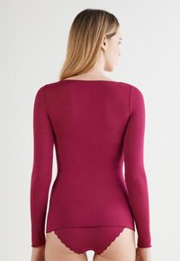 Langærmet top i dyb burgunder strikstof, med en rund halsudskæring og et tætsiddende design. Sættet er parret med matchende lace trim trusser.