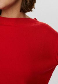 Indumento lavorato a maglia rosso che mostra una texture a coste, con una scollatura ampia e maniche corte, focalizzandosi sul colore vivace e sui dettagli del tessuto.
