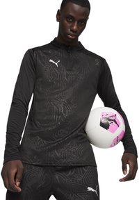 Schwarzes, langärmliges Sportoberteil mit dezentem geometrischem Muster, weißem Logo, kombiniert mit einem weißen Fußball, der pinke Akzente und Grafiken aufweist.