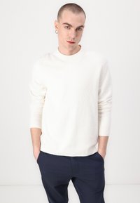 White textured sweater with long sleeves and a crew neck, paired with navy blue trousers. Soft material, slight stretch, and casual fit.