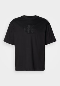 Crna majica kratkih rukava marke Calvin Klein s uzdignutim crnim logotipom "cK Calvin Klein" centriranim na prsima.