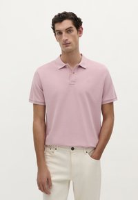 Polo rose clair avec un col et une patte de boutonnage �à trois boutons. Tissu doux, manches courtes, associé à un pantalon de couleur claire.