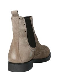 Stivaletto alla caviglia in suede color tortora con pannelli laterali elasticizzati, perforazioni decorative e suola in gomma nera. Presenta un piccolo inserto per il tallone sul retro.