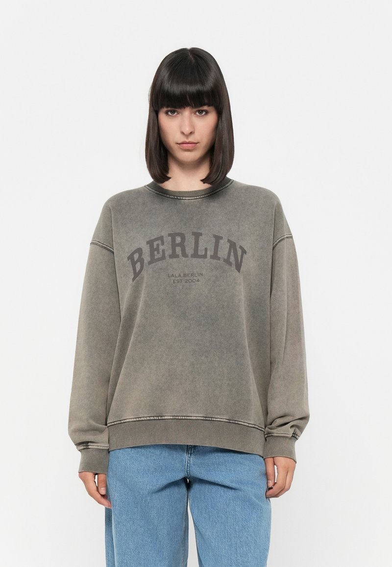 Felpa grigia corta con la scritta "BERLIN" stampata in marrone scuro, caratterizzata da polsini a costine, scollatura rotonda e una texture sbiadita.