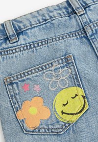 Poche en denim bleu avec des motifs floraux colorés et un visage souriant jaune imprimé sur le tissu.