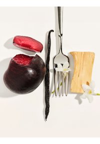 Ciruela morada oscura cortada por la mitad, vaina de vainilla, tenedor de plata con flor blanca, trozo de madera clara y flor blanca sobre fondo blanco.