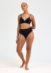 Set composto da reggiseno nero e bikini a vita alta realizzati in tessuto liscio. Il reggiseno presenta una scollatura profonda e spalline regolabili, con una fascia decorata con logo.