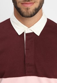 Bordeauxrode en lichtroze katoenen poloshirt met een witte, knoopsluitingkraag en een korte knoopsluiting met twee knopen en stikseldetail.