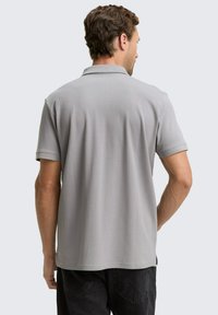 Grå polo T-shirt med korte ærmer, med en klassisk krave, glat tekstur og sidesprækker for bedre bevægelsesfrihed. Bagfra.