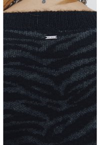 Pull en maille gris foncé avec un motif en vague texturé. L'étiquette visible sur le col indique "IKEA WOMEN." Matière douce et confortable.
