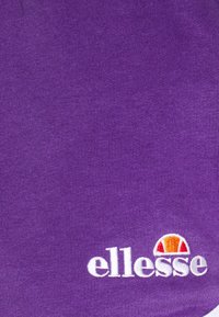 Tissu en coton violet arborant le logo "ellesse" en blanc, avec un accent de couleur arc-en-ciel au-dessus du texte. Texture lisse, couleur unie.