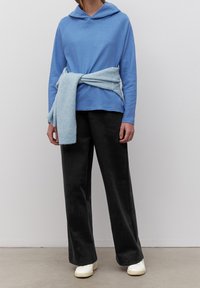 Ljusblå långärmad hoodie med en avslappnad passform, tillsammans med vida svarta byxor och en ljusblå scarf knuten i midjan. Vita sneakers.