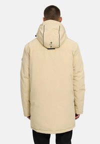 Beige isolerad parkas med huva, som har en hög krage, två sidofickor och svarta accenter i sömmarna. Slät textur.