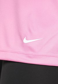 Camiseta deportiva rosa hecha de tejido suave, con un logo blanco de Nike en el dobladillo y costuras limpias, combinada con mallas negras.