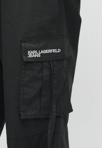 Juodi krovinių tipo kelnių pagaminti iš lengvos medžiagos, su šoniniu kišeniu ir siuvinėtu logotipu "KARL LAGERFELD JEANS."