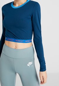 Navyblaues Langarm-Crop-Top mit hellblauem Kragen und "WORKOUT"-Bande, kombiniert mit hellgrauen, hochgeschnittenen Leggings mit einem weißen Logo.