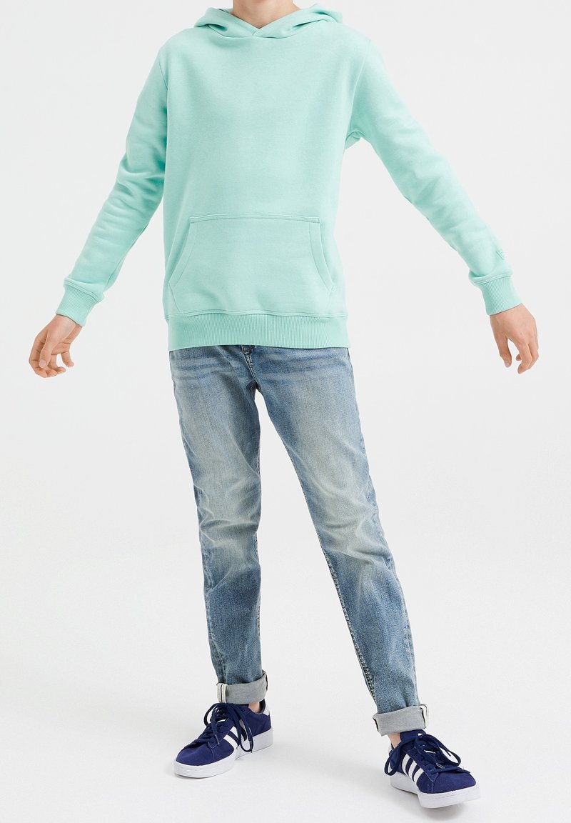 Sudadera verde menta con un bolsillo tipo canguro, puños acanalados y dobladillo; combinada con jeans de lavado claro, ligeramente desgastados y zapatillas de deporte azul marino.