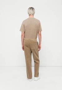 Tan cotton t-shirt and matching loose-fit corduroy pants with a back pocket, featuring an elastic waistband, styled with white sneakers.