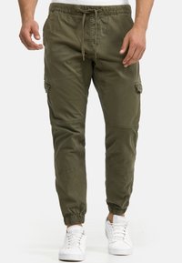 Pantaloni jogger verde măsliniu, realizați dintr-un material ușor, cu talie elastică, șnur de ajustare și buzunare cargo laterale. Se termină cu glezne mansetate.