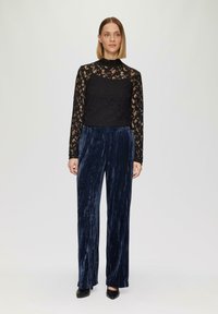 Zwarte kanten top met lange mouwen en een hoge hals, gecombineerd met marineblauwe fluwelen wijde broek. Gepunte zwarte hakken maken de outfit compleet.
