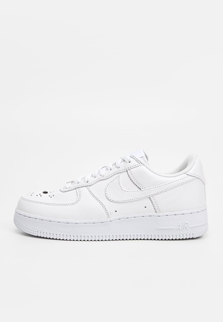 Zapatilla de cuero blanca de caña baja con puntera perforada, logo Swoosh bordado, cordones y suela de goma etiquetada con "Air" sobre fondo simple.