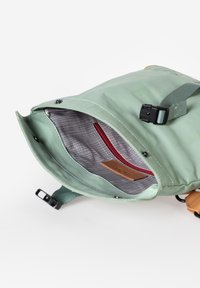 Borsa impermeabile verde con apertura superiore, foderatura interna in rete, una tasca rossa con zip e un'etichetta in pelle marrone chiaro. Includerà una tracolla regolabile.