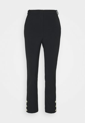 Pantalon noir taille haute, coupe slim, avec six boutons dorés — trois sur chaque cheville — sur un fond blanc uni.