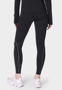 Zwarte leggings met een gladde textuur, voorzien van reflecterende stiksels langs de naden en een hoge tailleband voor een gestroomlijnde pasvorm.