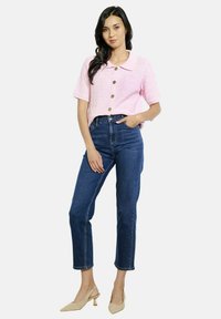 Heledad roosa lühikeste varrukatega kraega pluus tekstureeritud kangast, millel on kolm suurt nuppu, kombineeritud kõrge puusaga tumesiniste denimiste teksade ja nude värvi kontsadega.