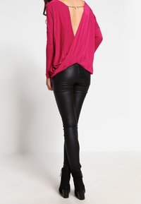 Fuchsia-langärmliges Oberteil mit tiefem V-Rücken und drapiertem Design, kombiniert mit schwarzen, gefälschten Lederleggings und schwarzen, hochhackigen Stiefeletten.