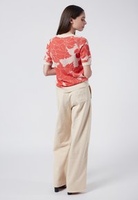 Short-sleeve sweater in coral and cream floral pattern, paired with beige wide-leg trousers. Sweater features ribbed collar and cuffs.