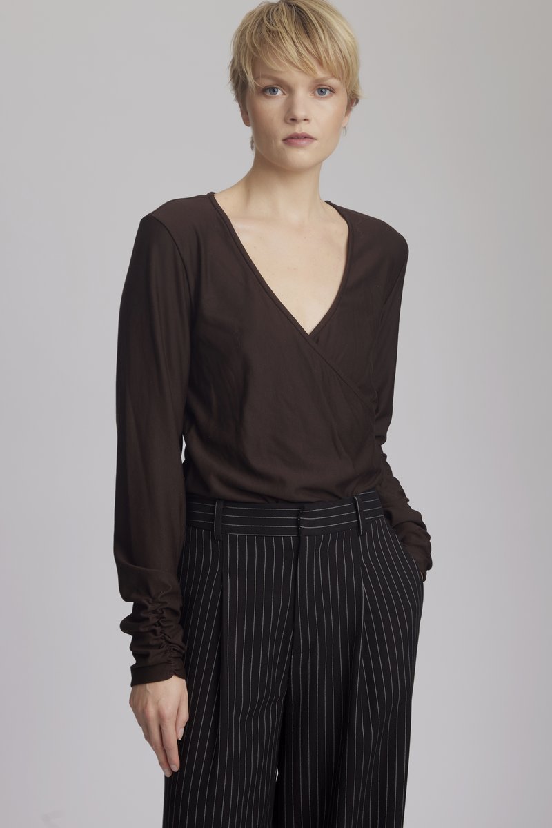 Brown long-sleeve wrap top with a deep V-neck, paired with black pinstriped high-waisted trousers. Smooth texture, fitted design.