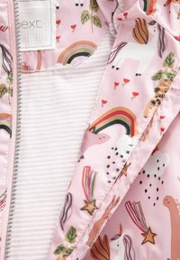 Ljusrosa jacka med ett färgglatt tryck av enhörningar, regnbågar och blommor. Interiören har ett randigt mönster. Dragkedjestängning.