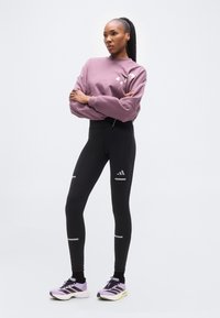 Μωβ φούτερ, μαύρο κολάν με ψηλή μέση και ανακλαστικές λεπτομέρειες, και παπούτσια τρεξίματος σε λιλά απόχρωση, με κομψό σχεδιασμό και αθλητικά υλικά.