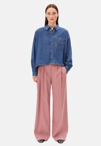 Denim button-up shirt in diepblauw met een borstzak, gecombineerd met high-waisted, wijdlopende broeken in zachtroze, met een gladde textuur.