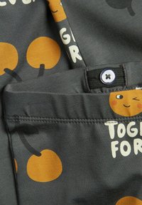 Grijs Kinderstof met gele lachende gezichten en oranje stippen, voorzien van een zwarte knoopdetail en een zijzak.