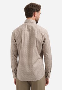 Lange mouwen shirt in lichtbeige met een geometrisch patroon. Heeft een kraag en een knoopsluiting, met manchetten bij de polsen.