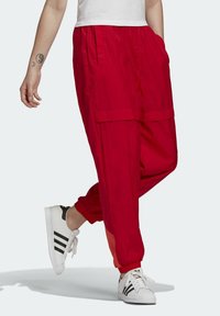 Röda lätta, löst sittande cargobyxor med två sidofickor och elastiska muddar, kombinerat med vita sneakers med svarta ränder.