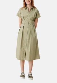 Šaty světle zelené barvy, délky po kolena, s krátkým rukávem, knoflíkovým zapínáním a skládací sukní, s pevně tvarovaným límečkem. Vysoké s sportovními zelenými teniskami.
