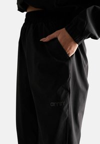 Jogger neri con vita elastica, dotati di tasca laterale, texture liscia e un discreto logo nella parte inferiore della gamba.