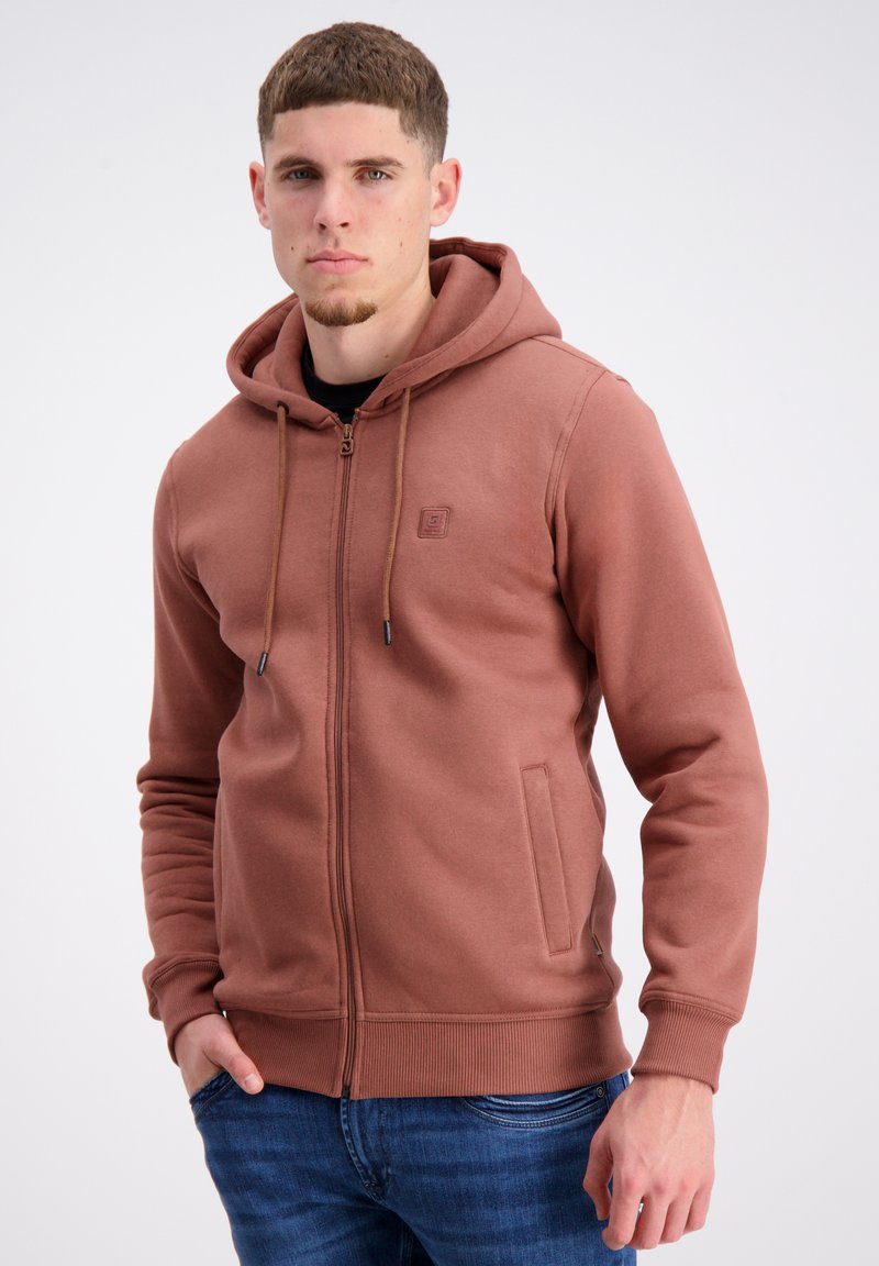 Brūns zip-up hoodie ar priekšējo kabatu, ar vadīklu kapuci un ribinātām piedurknēm. Gluda tekstūra un logo detaļa krūšu rajonā.
