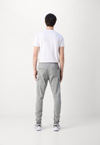 Szare spodnie cargo o tapered fit i elastycznym pasie, z wieloma kieszeniami i gładką teksturą materiału. Noszone z białym T-shirtem.