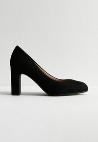 Scarpa nera in suede con tacco alto, punta arrotondata e tacco a blocco. La superficie ha una texture liscia, con un design semplice e classico.