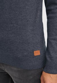 Donkerblauwe trui met geribde zoom en manchetten. Bevat een vierkant bruine leren label genaaid aan de zijkant met het woord "BLEND."