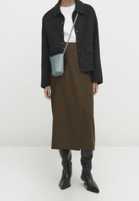 Schwarze Wollmischung Jacke, weißes T-Shirt, brauer Midi-Rock, schwarze knielange Stiefel und eine hellblaue Umhängetasche. Einfaches und funktionales Design.