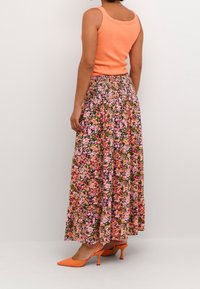 Débardeur orange assorti à une jupe longue fleurie aux tons rose, jaune et vert. Talons pointus orange complètent la tenue.