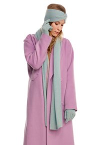 Cappotto di lana viola con due bottoni, abbinato a una sciarpa lavorata a maglia blu chiaro, guanti e fascia per capelli, che mostrano una texture morbida e un look a strati.
